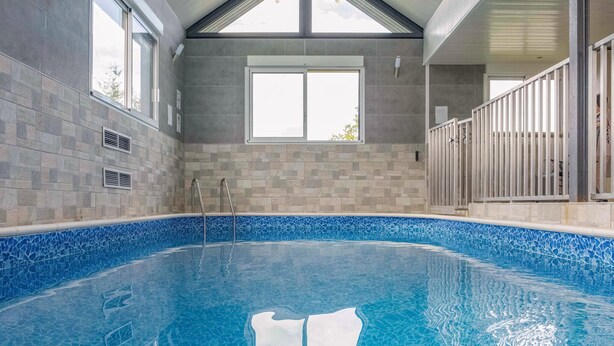 An indoor swimming pool with a tiled floor and walls, large windows, and a metal railing around the pool. - Cozy home in Villers-S/s-Foucarmont (Villers-S/s-Foucarmont)