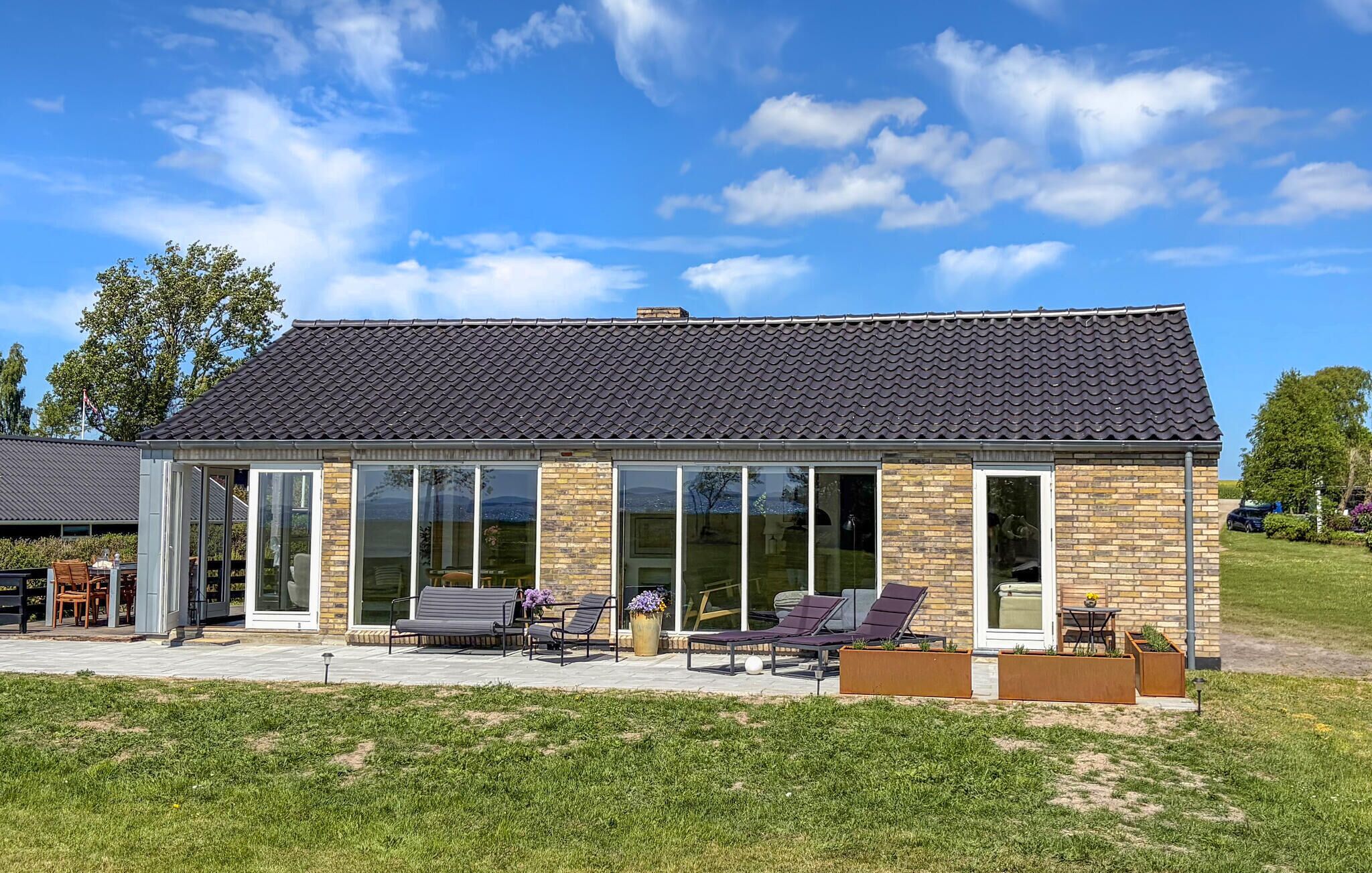 A modern house with a tiled roof, large glass windows, and outdoor seating.