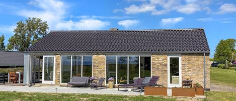 A modern house with a tiled roof, large glass windows, and outdoor seating.