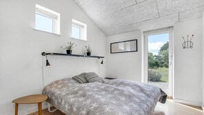 Ett sovrum med en säng, ett skrivbord, två fönster, ett tak med ett mönstrat utseende, en dörr som leder ut och en väggmonterad lampa.