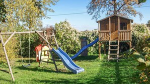 A wooden playhouse with a slide, a swing set, and a ladder leading to the roof. - 4 bedroom awesome home in Woldegk (Woldegk)