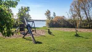 A park with a swing set, a sandy area, and a body of water in the background. - 4 bedroom awesome home in Woldegk (Woldegk)
