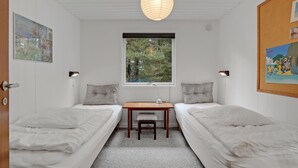 Una habitación pequeña y bien iluminada con dos camas individuales, una mesa de madera y ventana con vista a árboles.
