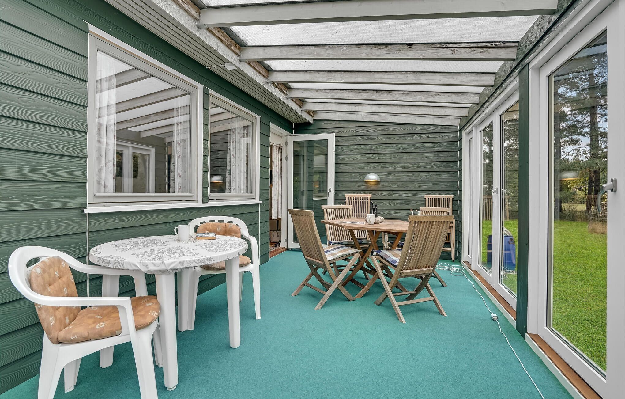 Een overdekt terras met een tafel en stoelen, een glazen deur naar buiten en uitzicht op de omgeving.