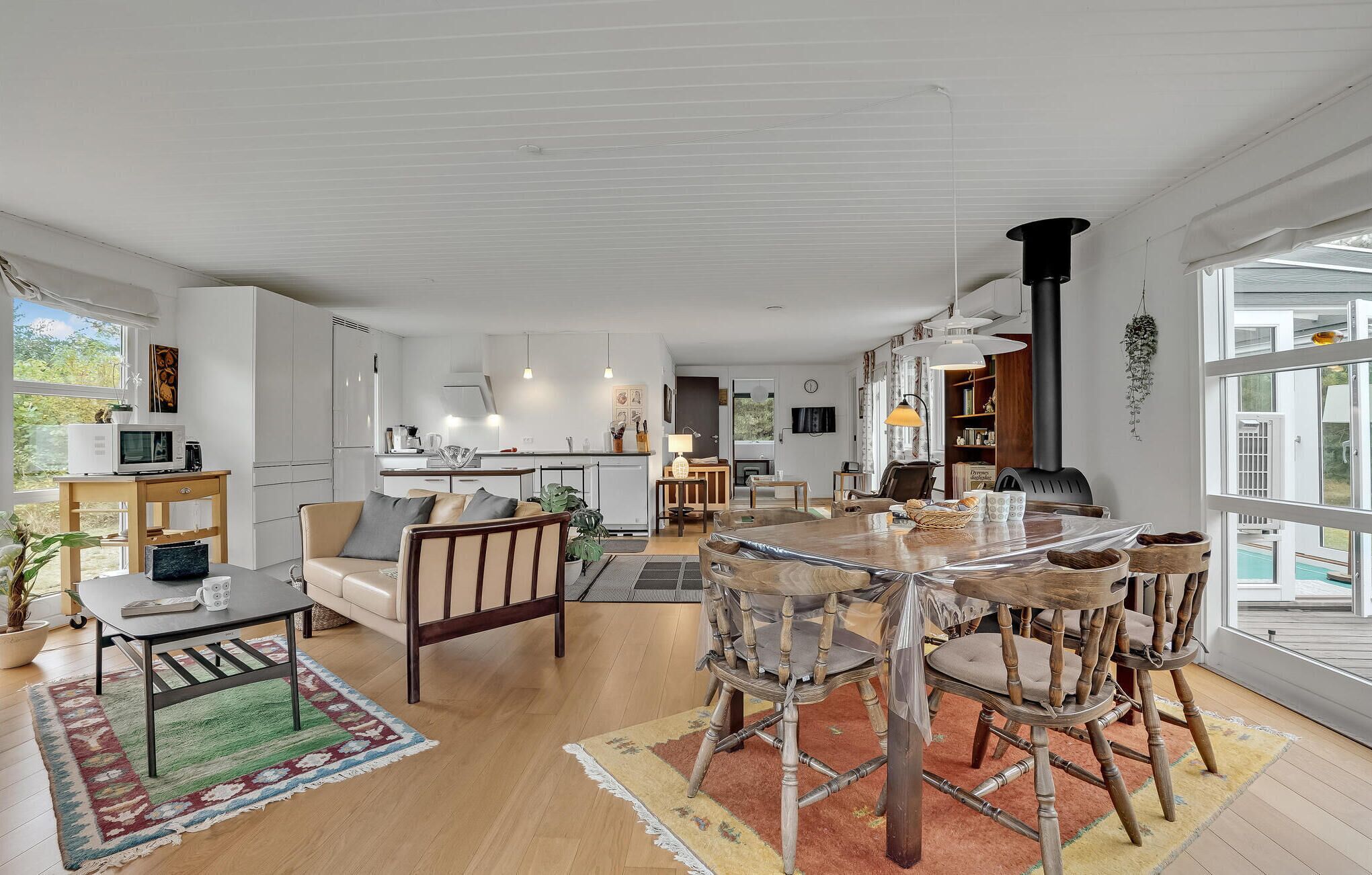A spacious living area with a large wooden dining table, multiple chairs, a sofa, and a kitchen in the background.