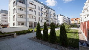 Een modern appartementencomplex met meerdere balkons, een verharde binnenplaats en netjes bijgesnoeid groen.