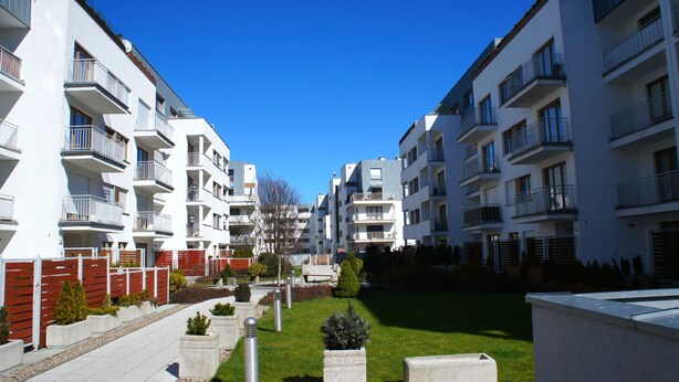 Een modern appartementencomplex met meerdere balkons, een centrale binnenplaats en een heldere blauwe lucht.