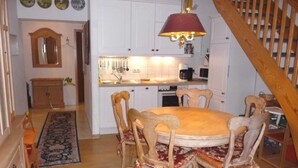 A dining area with a round wooden table and chairs, a chandelier, and a kitchen in the background. - (269) 3- room apartment - apartment house Strandburg (Kühlungsborn)