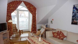 A living room with a sofa, armchair, TV, and a table with a floral tablecloth. - (269) 3- room apartment - apartment house Strandburg (Kühlungsborn)