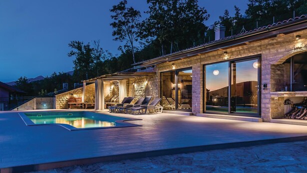 A modern outdoor pool area with stone walls, glass doors, and lounge chairs.