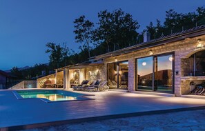 A modern outdoor pool area with stone walls, glass doors, and lounge chairs.