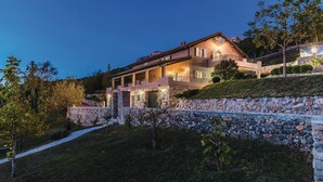 A multi-story house with a stone facade, a balcony, and a stone wall surrounding the property.