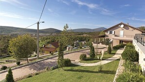 A residential area with a two-story house featuring a balcony, a paved driveway, and a stone wall.