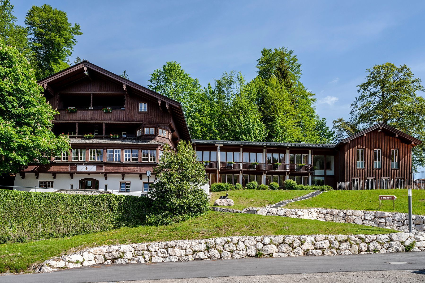 A multi-story wooden building with balconies, a stone wall, and a sign indicating 'Berghotel.'