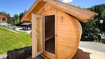 A wooden sauna with a door open, situated on a wooden deck.