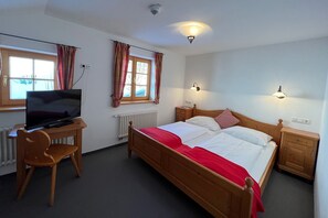 A bedroom with a bed, a desk with a TV, a chair, and two bedside tables with lamps.