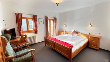 A bedroom with a wooden bed, a desk with a chair, a radiator, and two bedside lamps.