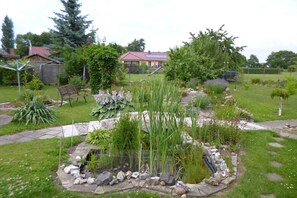 Un jardin avec un étang, un banc en bois et une maison en arrière-plan.