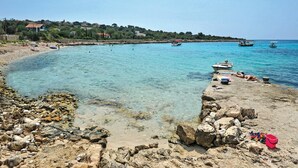 Una playa costera con agua turquesa cristalina, costa rocosa y barcos.