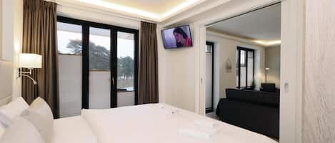 A hotel room with a large bed, a television mounted on the wall, a desk with a lamp, and a view of the outdoors through the window.