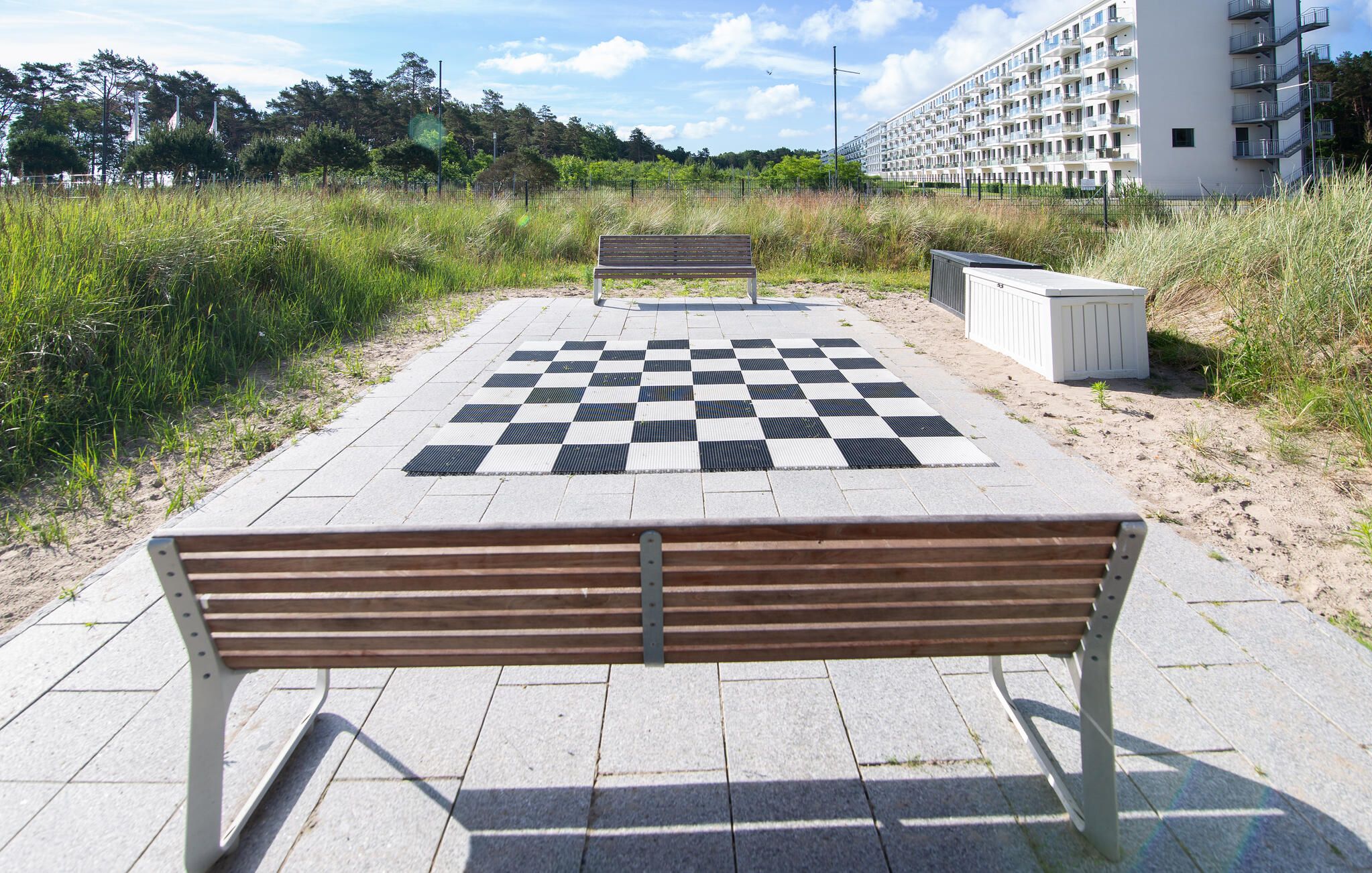Un espacio al aire libre con piso a cuadros, bancos, un edificio al fondo y una cerca.
