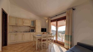 Eine kompakte Küche mit Esstisch und Stühlen, einer Couch und einem Balkon mit Vorhängen.