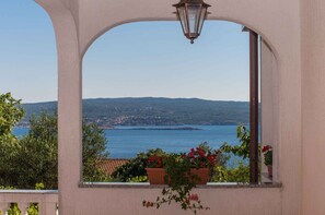 A view through an arched window with a lamp, overlooking a body of water and distant hills.