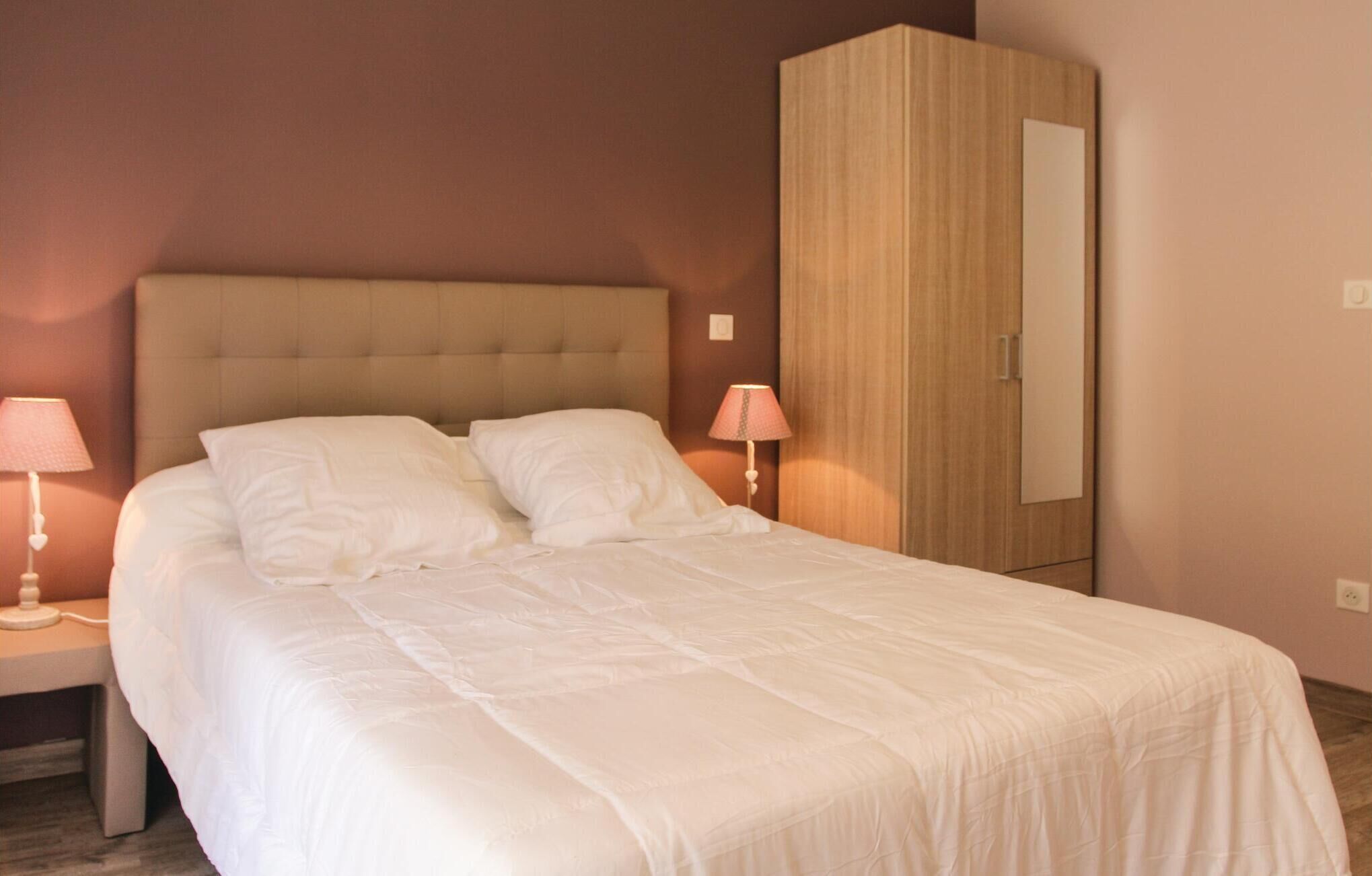 A neatly made bed with white linens, a wooden wardrobe, and two bedside lamps.