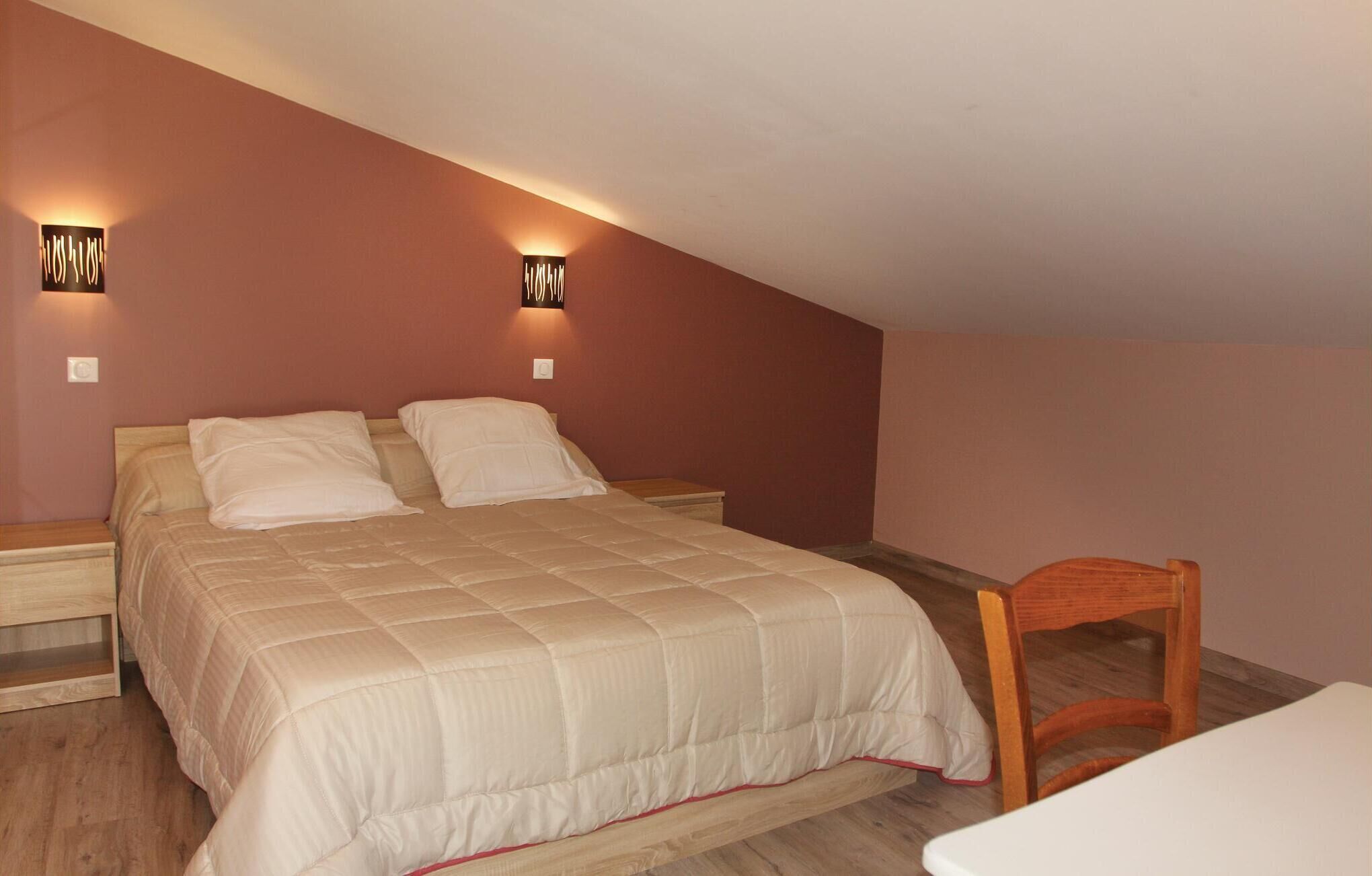 A bedroom with a bed, two wall-mounted lights, a wooden nightstand, and a wooden chair.