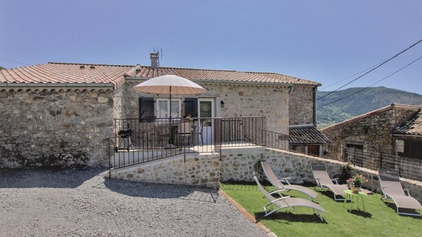 A stone building with a tiled roof, a balcony with a table and chairs, and a small garden area with sun loungers. - 2 bedroom stunning home in St Etienne de Boulogne (St Etienne de Boulogne)