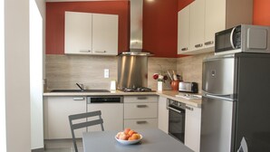 A modern kitchen with white cabinets, a stainless steel range hood, a microwave, a toaster, and a refrigerator. There is a table with a bowl of fruit and a chair. - 2 bedroom stunning home in St Etienne de Boulogne (St Etienne de Boulogne)