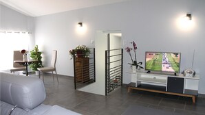 A modern living room with a sofa, a TV, and a dining area with a table and chairs. - 2 bedroom stunning home in St Etienne de Boulogne (St Etienne de Boulogne)