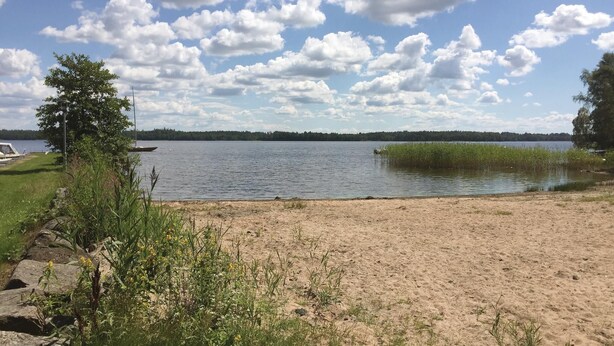 A lakeside view with a sandy beach, a boat, and a forested shoreline. - Cozy home in Bolmsö with WiFi (Bolmsö)