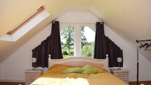 A bedroom with a sloped ceiling, a bed with a yellow bedspread, two bedside tables, a nightstand, a lamp, and a window with curtains. - Cozy home in Bolmsö with WiFi (Bolmsö)