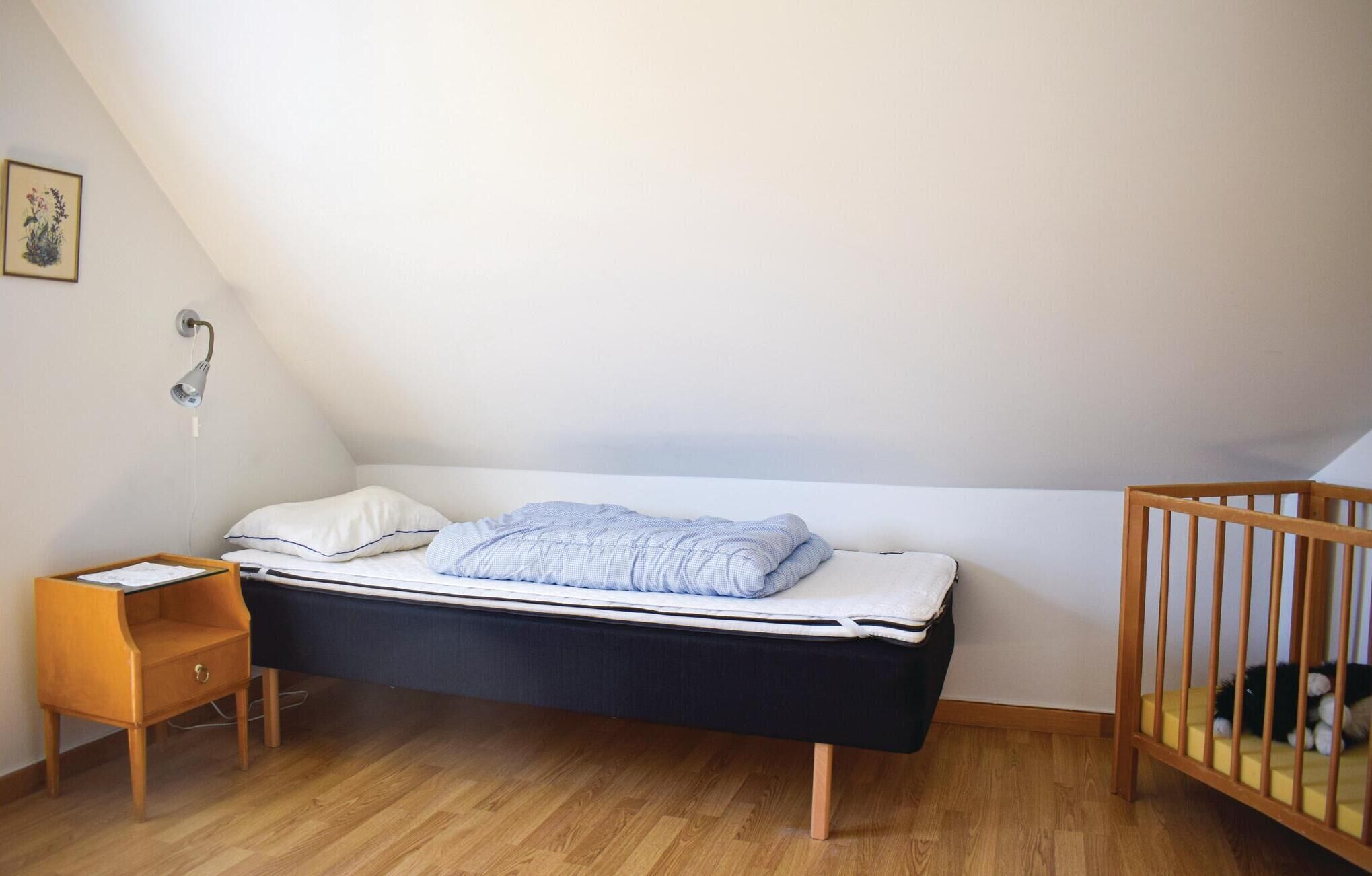 Un dormitorio pequeño y ordenado con una cama individual, una mesita de noche, una silla de madera y una cuna.