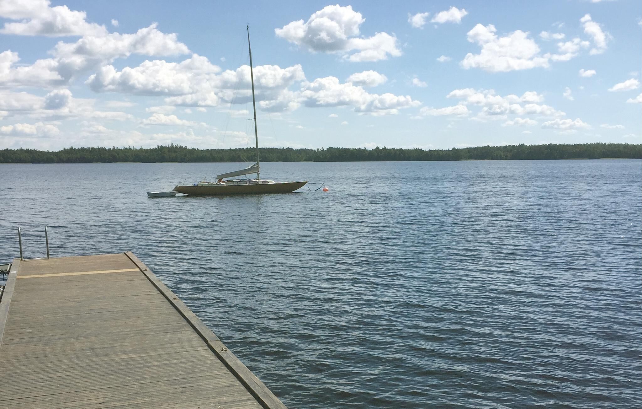 Un muelle de madera se extiende sobre aguas tranquilas, con un velero anclado cerca.