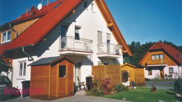 A two-story house with a red roof, a balcony, and a small attached garage. - (123) 3-room apartment - Apartments Leuchtturmblick (Kühlungsborn)