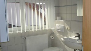 A small, clean bathroom with a toilet, sink, and window with blinds. - (123) 3-room apartment - Apartments Leuchtturmblick (Kühlungsborn)