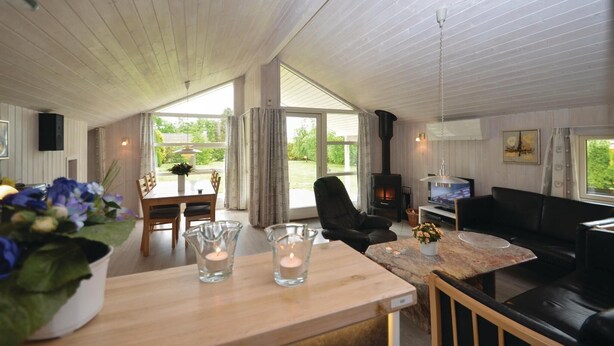 A spacious living room with a fireplace, a dining area with a table and chairs, and large windows offering a view of the outdoors. - Beach front home in Væggerløse with sauna (Væggerløse)