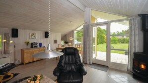 A modern living room with a fireplace, a dining area, and a large sliding glass door leading to a garden. - Beach front home in Væggerløse with sauna (Væggerløse)