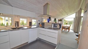 A modern kitchen with white cabinets, a built-in dishwasher, and a large window. - Beach front home in Væggerløse with sauna (Væggerløse)