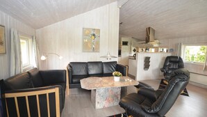 A modern living room with a black leather sofa, a marble coffee table, and a black leather armchair. There is a kitchen area in the background with a white refrigerator and a microwave. - Beach front home in Væggerløse with sauna (Væggerløse)