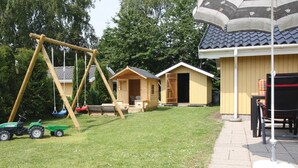 A wooden cabin with a swing set and a covered outdoor seating area. - Beach front home in Væggerløse with sauna (Væggerløse)