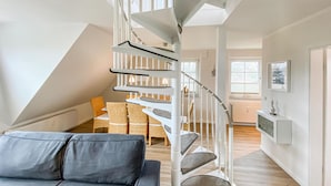 Ein modernes Loft mit Wendeltreppe, einer gemütlichen Sitzecke mit grauem Sofa und einem Essbereich mit Korbstühlen.