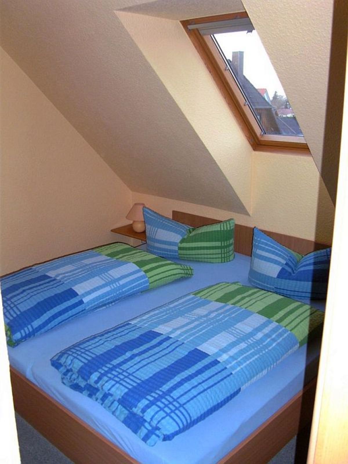 A bedroom with a sloped ceiling, a skylight, a bed with striped bedding, and a bedside table with a lamp.
