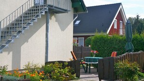 Un immeuble résidentiel doté d’un escalier, d’un balcon, d’une table avec des chaises et d’un jardin.