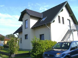 A two-story house with a steeply pitched roof, a visible staircase, and a parked car in the foreground. - Rügen-Fewo 192 - Apartment (Glowe)