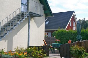 A residential building with a staircase, a balcony, a table with chairs, and a garden. - Rügen-Fewo 192 - Apartment (Glowe)