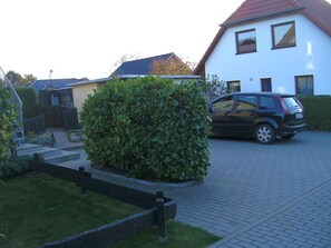 A residential area with a paved driveway, a parked car, and a white house with a red roof. - Rügen-Fewo 192 - Apartment (Glowe)