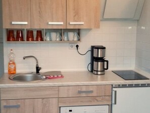 A kitchen with wooden cabinets, a stainless steel coffee maker, a sink, and a dishwasher. - Rügen-Fewo 192 - Apartment (Glowe)